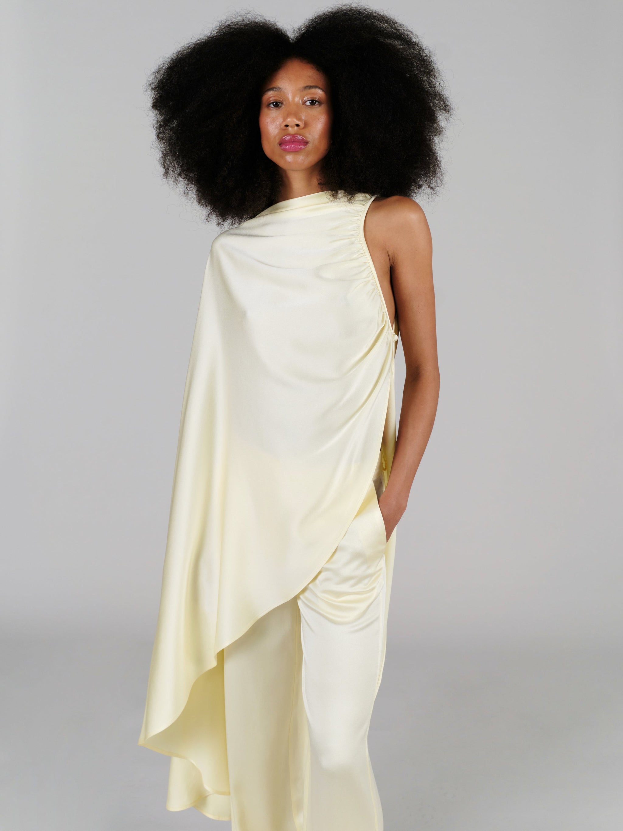Woman wearing a light yellow draped outfit against a gray background