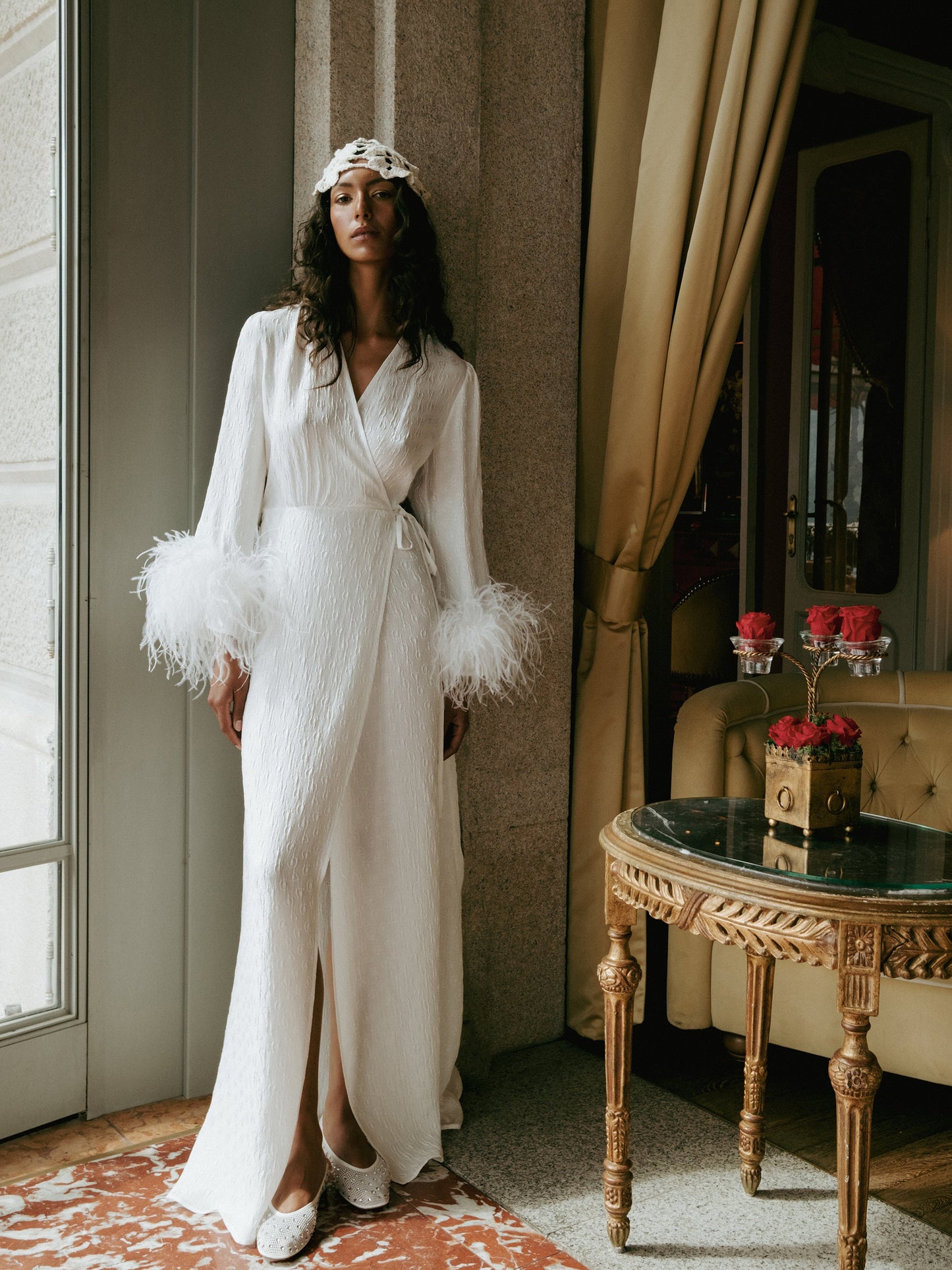 Woman in a white dress with feathered sleeves standing in an elegant room.
